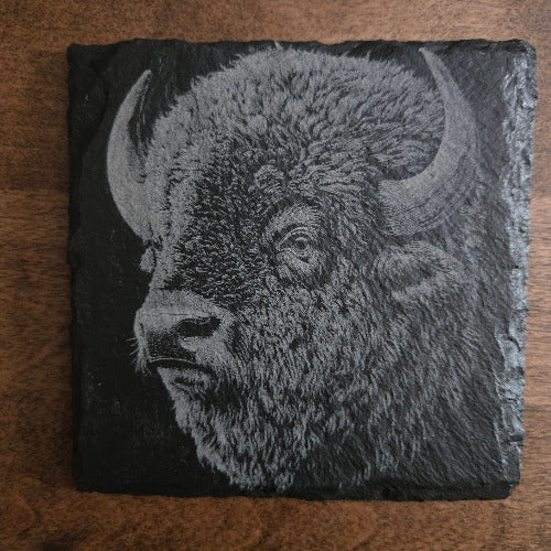 Slate coaster with engraved bison design on a wooden surface