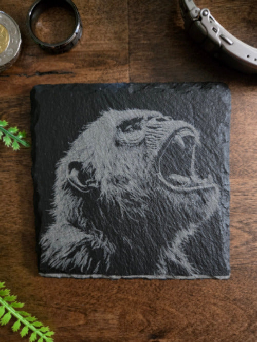 Slate coaster with an ape engraving on a wooden surface
