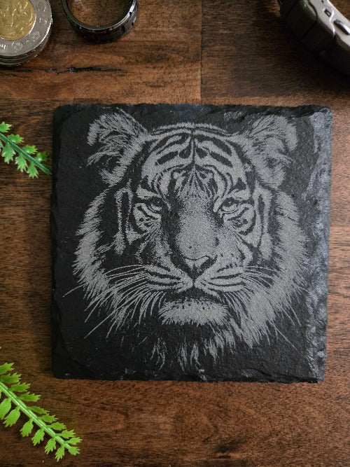 Slate coaster with a engraved tiger design on a wooden surface
